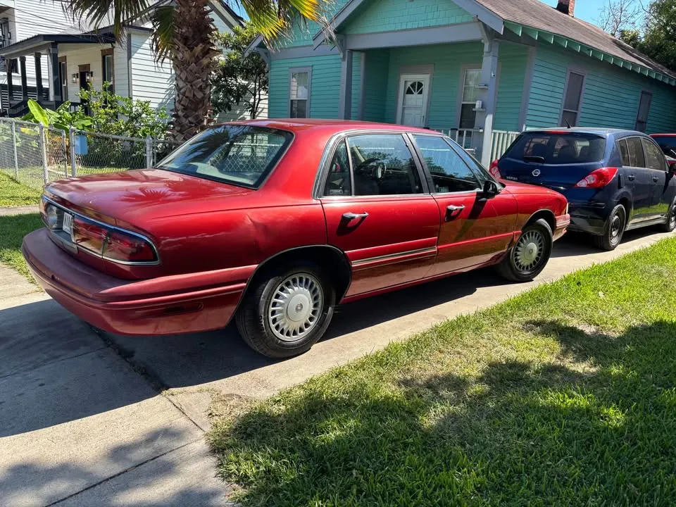 Red 1997 Buick LeSabre Limited parked at the curb outside a Texas bungalow