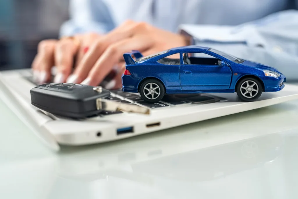 Working at a laptop on Pennsylvania online vehicle services with a model car on the desk