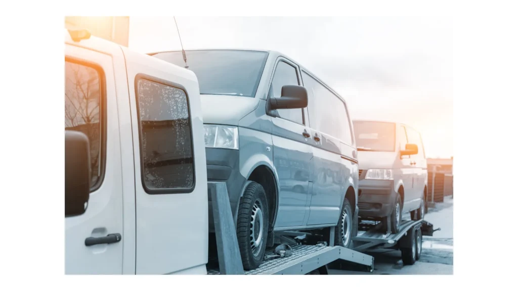 White small cargo truck car carrier loaded with two yellow van minibus on flatbed platform and semi trailer tow on roadside highway road